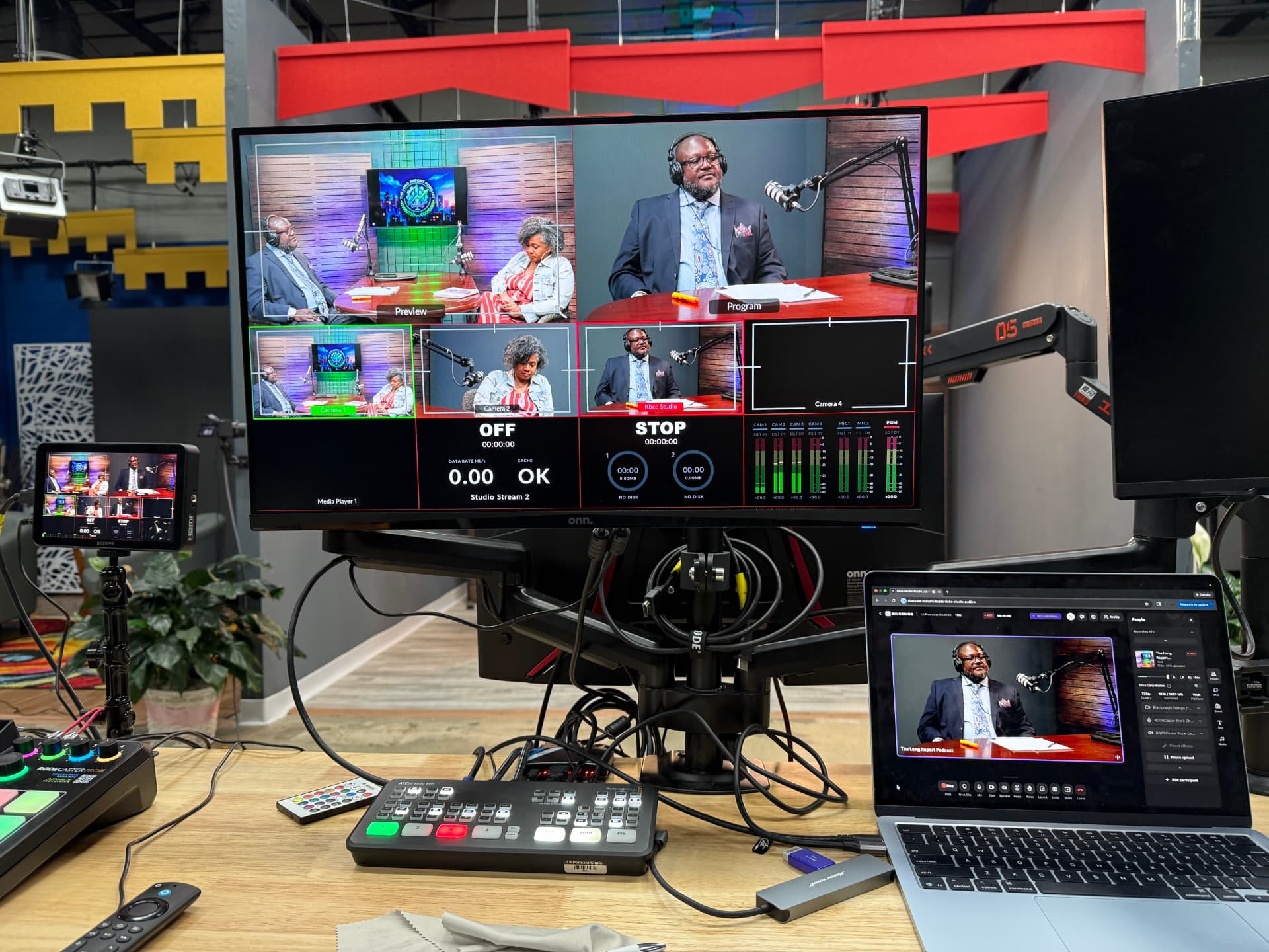 Multi-camera production cart with a video switcher, broadcast monitors, and laptop showing a live podcast recording